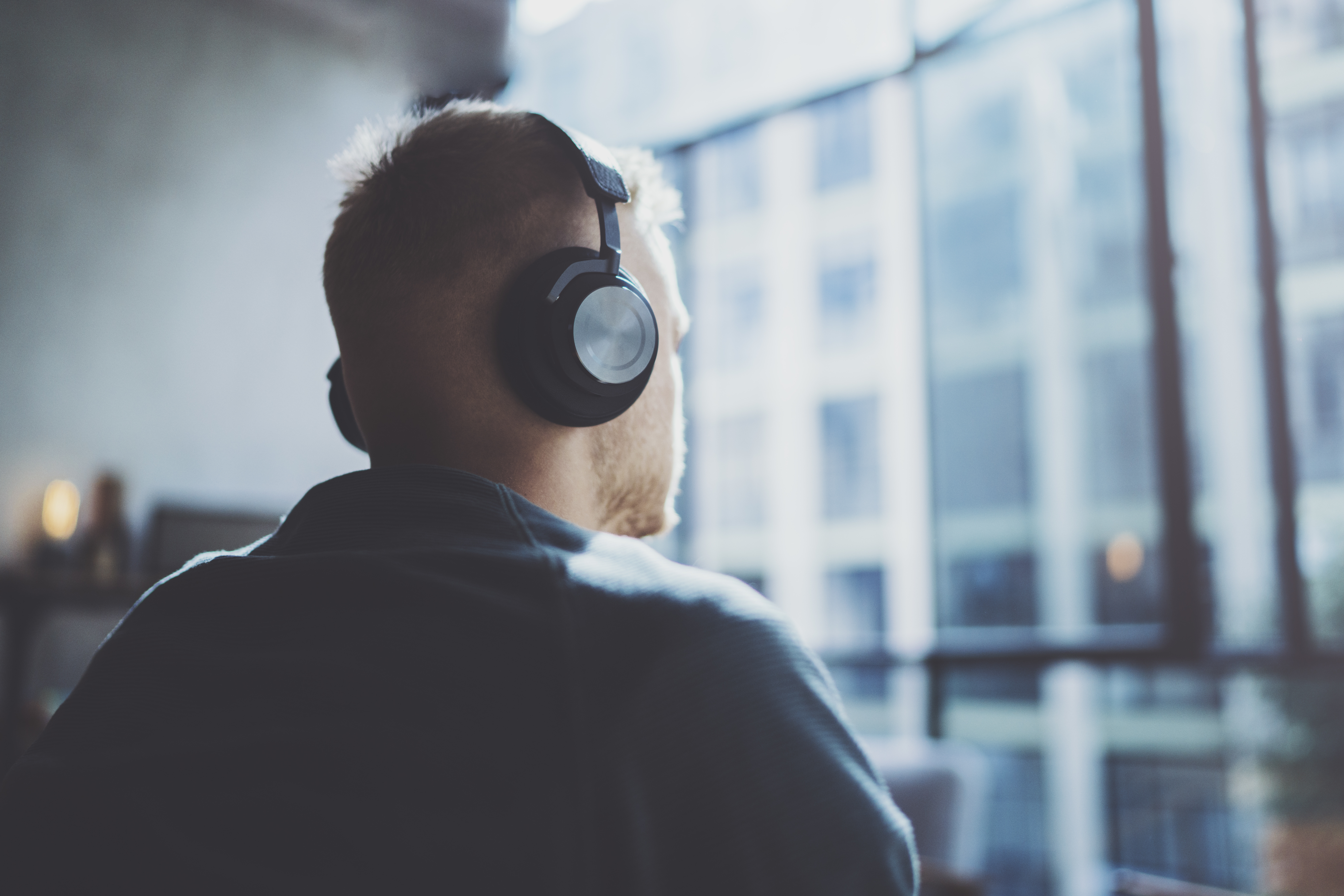 Attractive young man wearing glasses casual clothes.Man sitting in vintage armchair modern loft studio and relaxing whith headphone music.Panoramic windows on blurred background.Horizontal.